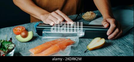 un jeune homme caucasien est l'emballage sous vide de deux morceaux de saumon dans un sac transparent, dans un format panoramique à utiliser comme bannière web ou en-tête Banque D'Images