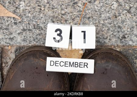 31 décembre écrit sur des cubes en bois se trouve sur des bottes d'hiver sur une route en pierre sur la rue en hiver, bonne année, calendrier et temps, papier peint Banque D'Images