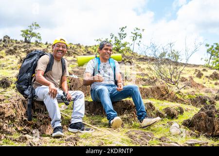 Randonneurs souriants heureux ou voyageurs avec sac à dos regarder l'appareil photo tout en trekking sur la montagne - concept d'amitié, de détente et de loisirs Banque D'Images