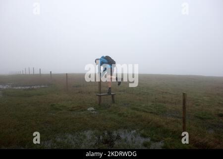 Homme grimpant sur une dalle de bois au-dessus de Wire Fence, près du sommet de la colline de la Grande Knotberry, dans le parc national des Yorkshire Dales, dans le nord du Yorkshire, en Angleterre, au Royaume-Uni. Banque D'Images