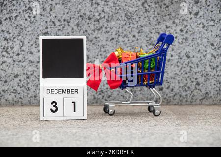 31 décembre est écrit sur une plaque de bois dans le calendrier, et à côté de lui est un panier d'un supermarché avec des cadeaux dans la rue, bonne année, nouveau vous Banque D'Images