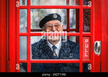 Londres, Royaume-Uni. 08th novembre 2022. Un vétéran de l'armée britannique sourit alors qu'il se protège de la forte pluie dans une boîte téléphonique rouge de Londres sur Whitehall près du Cenotaph. Credit: Imagetraceur/Alamy Live News Banque D'Images