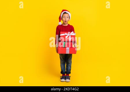 Pleine photo de mignon petit garçon impressionné beaucoup de cadeaux de noël Nord pole porter tendance rouge look isolé sur fond jaune couleur Banque D'Images