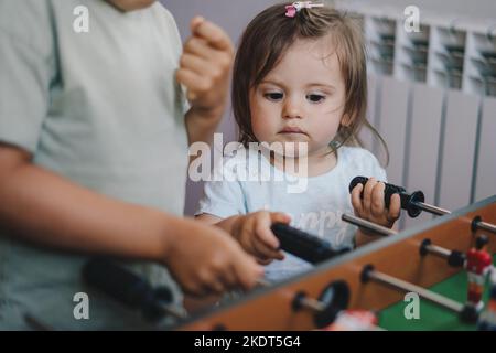 La jeune sœur de bébé regarde avec admiration comment son frère joue au baby-foot. Concept de travail d'équipe. Concept football. Développement des enfants Banque D'Images