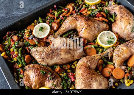 Des cuisses de poulet rôties avec des légumes mélangés sur une plaque de cuisson isolée sur fond sombre par le dessus Banque D'Images