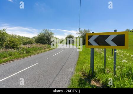 Un panneau à chevron noir et blanc signale un virage à gauche sur Cliff Road au sommet de la gorge de Cheddar dans les Mendip Hills, Somerset, Angleterre. Banque D'Images