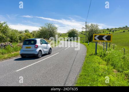 Circulation passant un panneau noir et blanc à chevron indiquant un virage à gauche sur Cliff Road au sommet de la gorge de Cheddar dans les Mendip Hills, Somerset, Angleterre. Banque D'Images