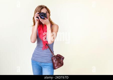 Jeune femme à tête rouge regardant à travers le viseur avec un ancien appareil photo reflex 35mm. Banque D'Images