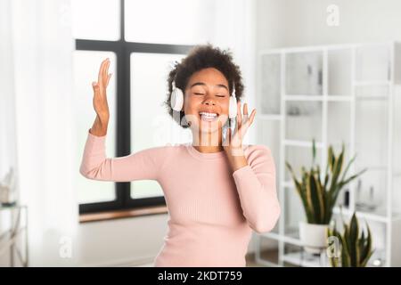 Bonne femme afro-américaine millénaire en casque sans fil chante, aime la musique préférée Banque D'Images