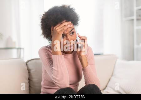 Triste effrayé choqué frustré femme afro-américaine millénaire, appel et parler par téléphone intelligent, souffrent de stress Banque D'Images