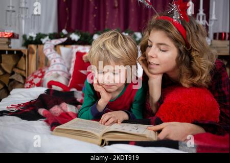 La veille de Noël à la maison avec la famille. La sœur aînée et le frère cadet sont couché en pyjama sur le lit et la lecture d'un livre. Concept d'amitié, mut Banque D'Images