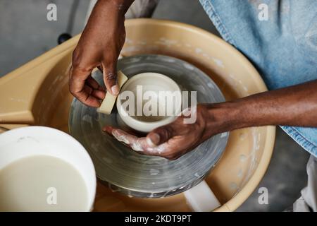 Vue de dessus des mains masculines d'un jeune homme noir utilisant la roue de poterie et créant des céramiques faites à la main Banque D'Images