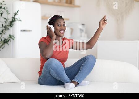 Passe-temps favori. Une femme noire joyeuse écoute de la musique dans un casque sans fil à la maison Banque D'Images