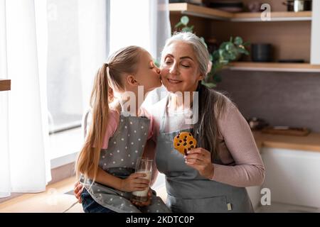 Souriante petite-fille caucasienne embrasse la grand-mère âgée sur la joue avec des biscuits, profiter de la cuisson Banque D'Images