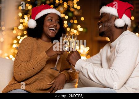 Joyeux millennium noir dame et homme dans les chapeaux de Santa, des acclamations avec des verres de champagne, profiter des vacances Banque D'Images