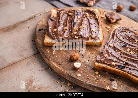 Planche de pain avec pâte de chocolat et bonbons de fête saupoudrer et noisettes sur fond de bois. Nourriture populaire de dessicer. Vue de dessus. Banque D'Images