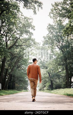 Un jeune homme beau marche le long d'une large route avec d'énormes arbres Banque D'Images