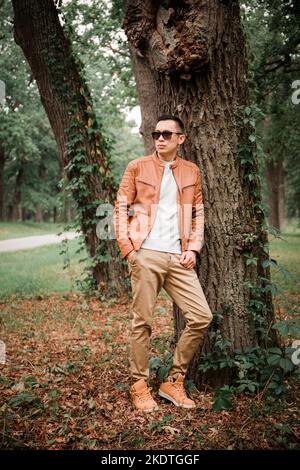 Un jeune homme beau se tient sous un arbre dans un parc d'automne Banque D'Images