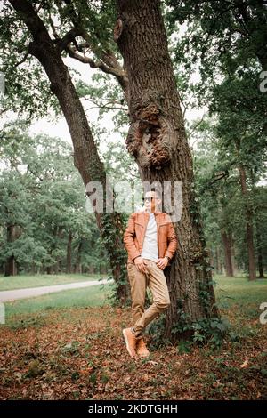 Un jeune homme beau se tient sous un arbre dans un parc d'automne Banque D'Images