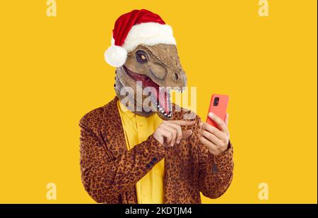 Homme drôle portant un masque de dinosaure, un chapeau de Noël et un costume de léopard en utilisant un téléphone portable Banque D'Images