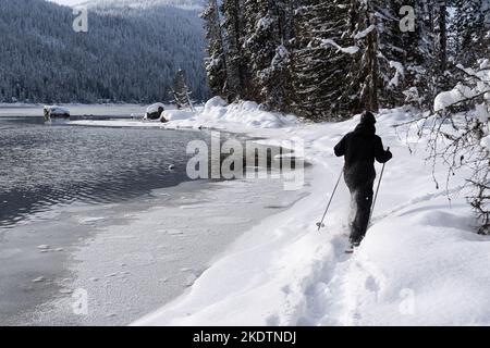 Homme raquette à travers la neige le long du lac partiellement gelé en hiver Banque D'Images