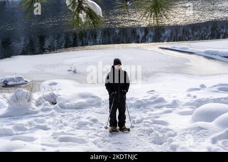 Homme raquette le long du lac partiellement gelé en hiver Banque D'Images