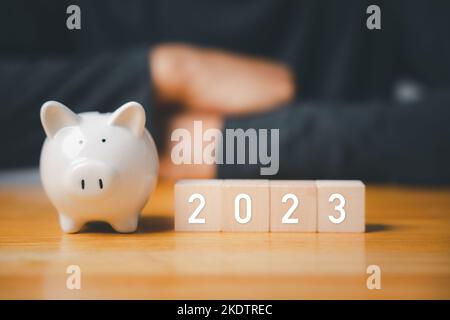 Homme d'affaires avec des cubes de bois bloc années 2023 et la banque de piggy Banque D'Images