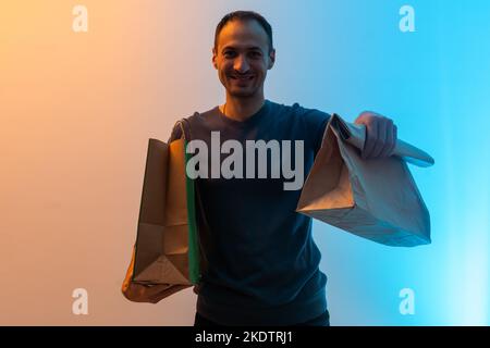 Le liveur tient le paquet de papier d'artisanat avec de la nourriture sur un fond bleu. Portrait de la nourriture de livraison d'homme beau Banque D'Images
