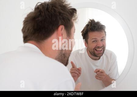 Homme essayant de s'encourager à montrer le pouce vers le haut regardant dans le miroir. Banque D'Images