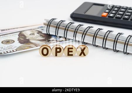 Concept d'entreprise. Sur une surface blanche sont des dollars, un carnet, une calculatrice et des cercles en bois avec l'inscription - OPEX Banque D'Images