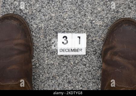 31 décembre est écrit sur des cubes de calendrier en bois qui se trouvent sur une pierre grise et des chaussures d'hiver marron stand à proximité dans la rue, bonne année, vacances Banque D'Images