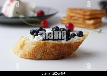 Un gros plan de sandwichs aux myrtilles sur fond blanc avec fromage de cerise et gaufres à l'arrière-plan. Un délicieux petit déjeuner sain et correct. Banque D'Images