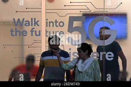 Un homme et une femme sortent d'un magasin de fournisseur de services mobiles annonçant le service 5G à Mumbai. 5G est la cinquième génération de technologie cellulaire, cent fois plus rapide que 4G, ce qui contribuera à créer des opportunités pour les gens et les entreprises. Banque D'Images