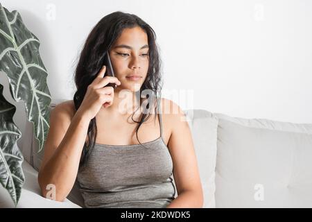 latina brune femme assise sur le canapé à la maison recevant un appel, avec un visage très sérieux Banque D'Images