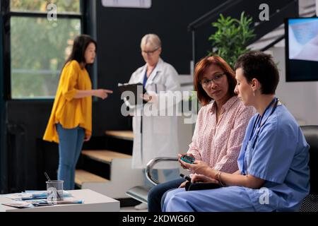 Médecin infirmier mesurant le taux d'insuline et de glucose dans l'échantillon sanguin à l'aide de glucomètre, consultant patient asiatique avec le diabète. Assistant faisant un test médical avec une femme diabétique, visite de contrôle. Banque D'Images