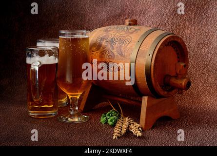Trois verres différents avec bière légère, à côté d'un fût en bois, houblon et oreilles d'orge sur fond marron abstrait. Gros plan. Banque D'Images