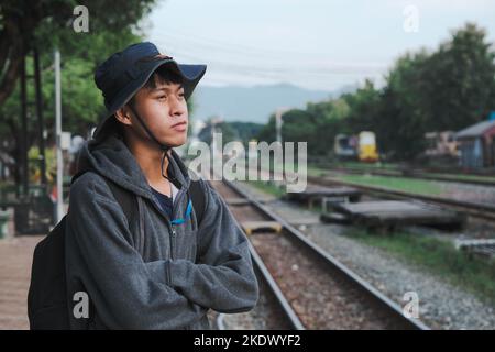 Un jeune homme se tient sur une plate-forme à une gare et prend une photo. Le gars se tient près des voies de chemin de fer pour voyager. Voyages et transport Banque D'Images