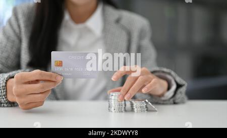 Belle femme asiatique tenant une carte de crédit, pile de pièces d'argent sur la table. Gros plan image. finance, banque, argent, monnaie, investissement Banque D'Images