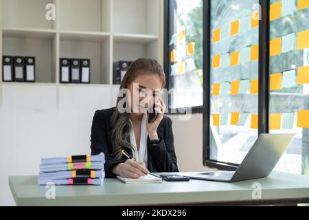 Portrait comptable d'affaires asiatique femme appelant au téléphone et prenant des notes Banque D'Images