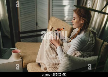 Jolie dame avec les yeux patchs à la maison écrivant des notes sur un journal tout en se relaxant prendre une pause, appréciant le style de vie à la maison. Repos, vacances, beauté Banque D'Images