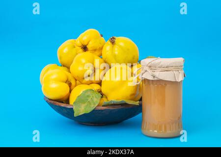 Pile de fruits de Quince dans un bol en bois, avec une confiture sans étiquette, mise au point douce de près isolée sur fond bleu Banque D'Images