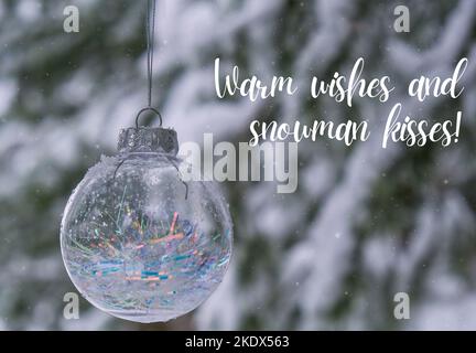 Voeux chaleureux et bonhomme de neige inspiration plaisanterie citation phrase transparent tendance verre boule de Noël sur la neige branche ferme dans la forêt d'hiver. Arrière-plan des vacances d'hiver. Bonne année carte de vœux de joyeux Noël. Chute de neige en arrière-plan Banque D'Images