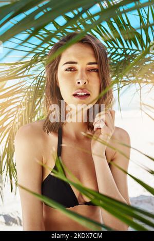 Rien de plus sexy qu'une chaude journée d'été. Une jeune femme attrayante debout sous l'ombre d'un palmier à la plage. Banque D'Images