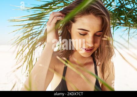 La meilleure façon de passer une journée chaude d'été. Une jeune femme attrayante debout sous l'ombre d'un palmier à la plage. Banque D'Images