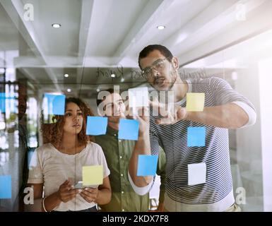 Prendre l'initiative. Un groupe de jeunes designers planifiant sur une planche de verre. Banque D'Images