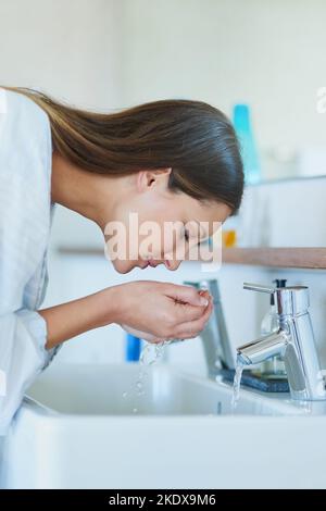 Elle se réveille avec un jet d'eau. Une jeune femme lavant son visage sur le lavabo de la salle de bains à la maison. Banque D'Images