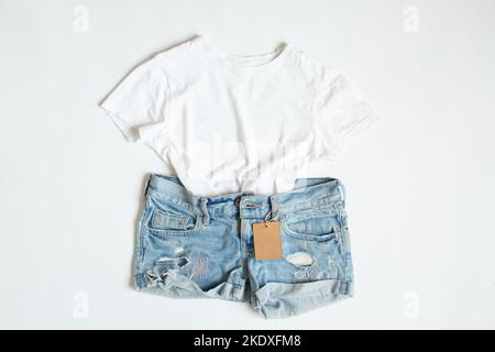 Un t-shirt blanc et un short en denim se trouvent sur un fond blanc avec une étiquette de prix, une vente de vêtements, un magasin d'affaires et de vêtements Banque D'Images