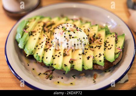 De dessus de toasts appétissants avec des tranches d'avocat et des œufs pochés parsemés de graines de chia servi sur une plaque en céramique placée sur une table en bois Banque D'Images