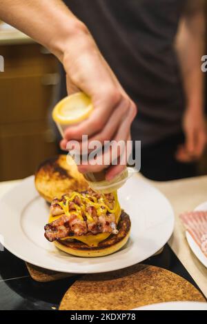 De dessus crop anonyme chef mâle debout près de la table et verser le hamburger frais cuit juteux avec la moutarde de la bouteille Banque D'Images