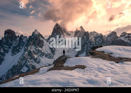 Vue arrière d'un touriste méconnaissable en vêtements de dessus debout sur la neige et observant les pics de Tre cime di Lavaredo contre ciel nuageux ensoleillé dans les Dolomites, il Banque D'Images